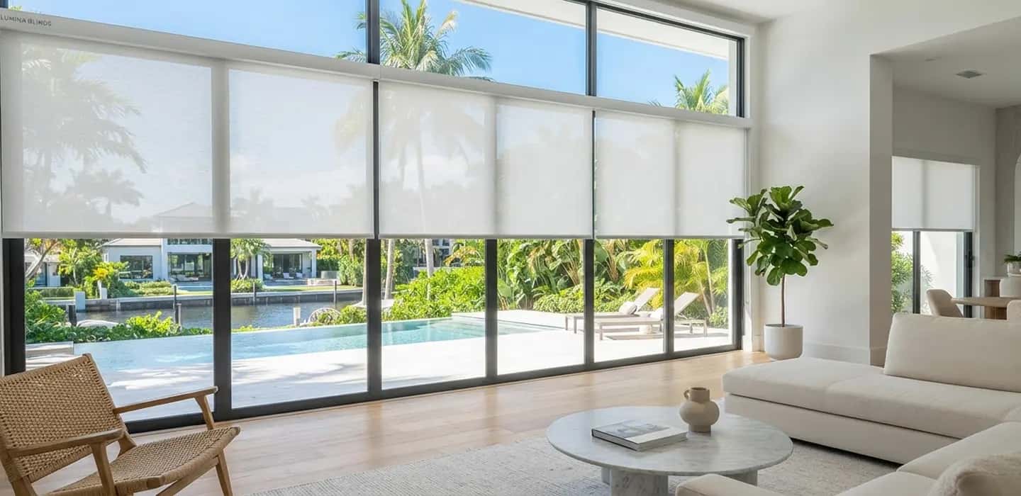 Modern living room with floor-to-ceiling windows fitted with roller blinds, palm trees and a pool visible outside